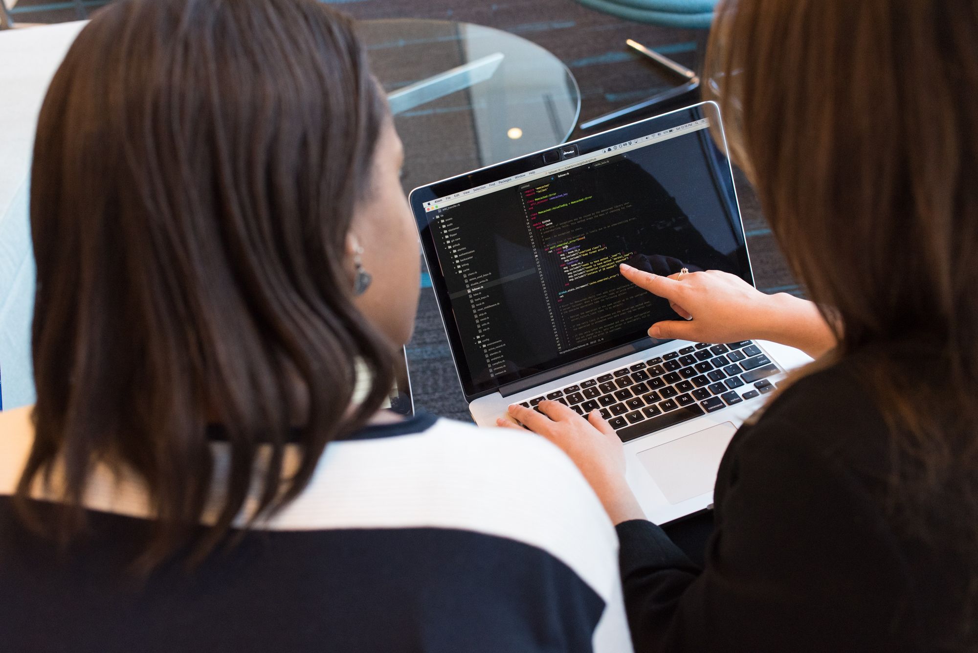 Two developers talking and pointing at laptop with code on screen