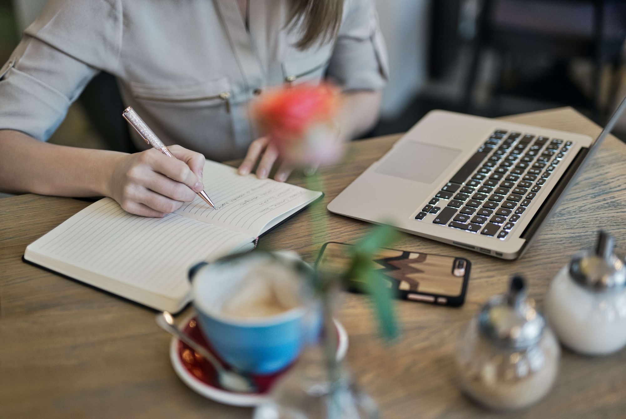 woman writing on notebook with a laptop nearby